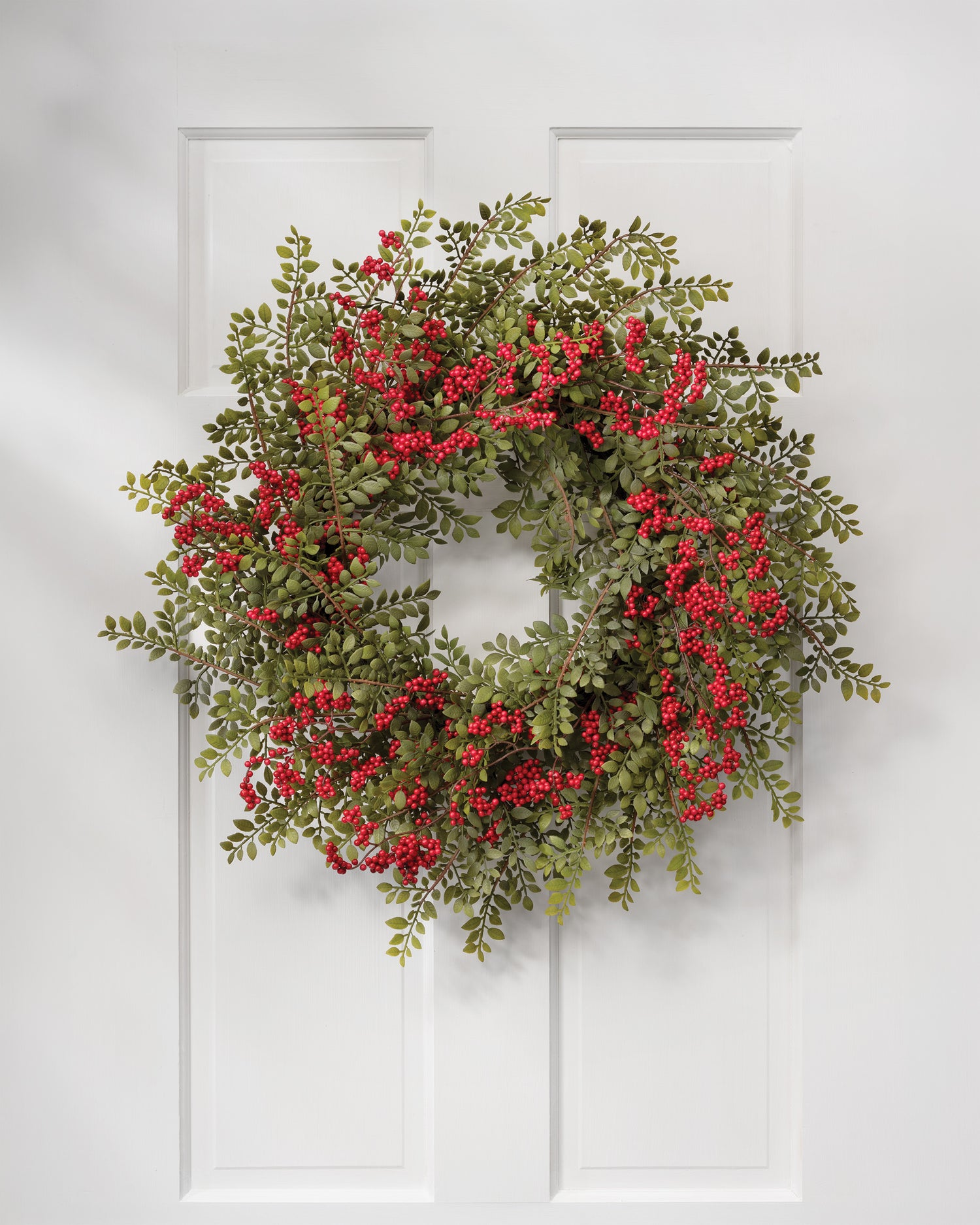 24" Ruscus & Berry Faux Christmas Wreath, hanging on a white wooen door.