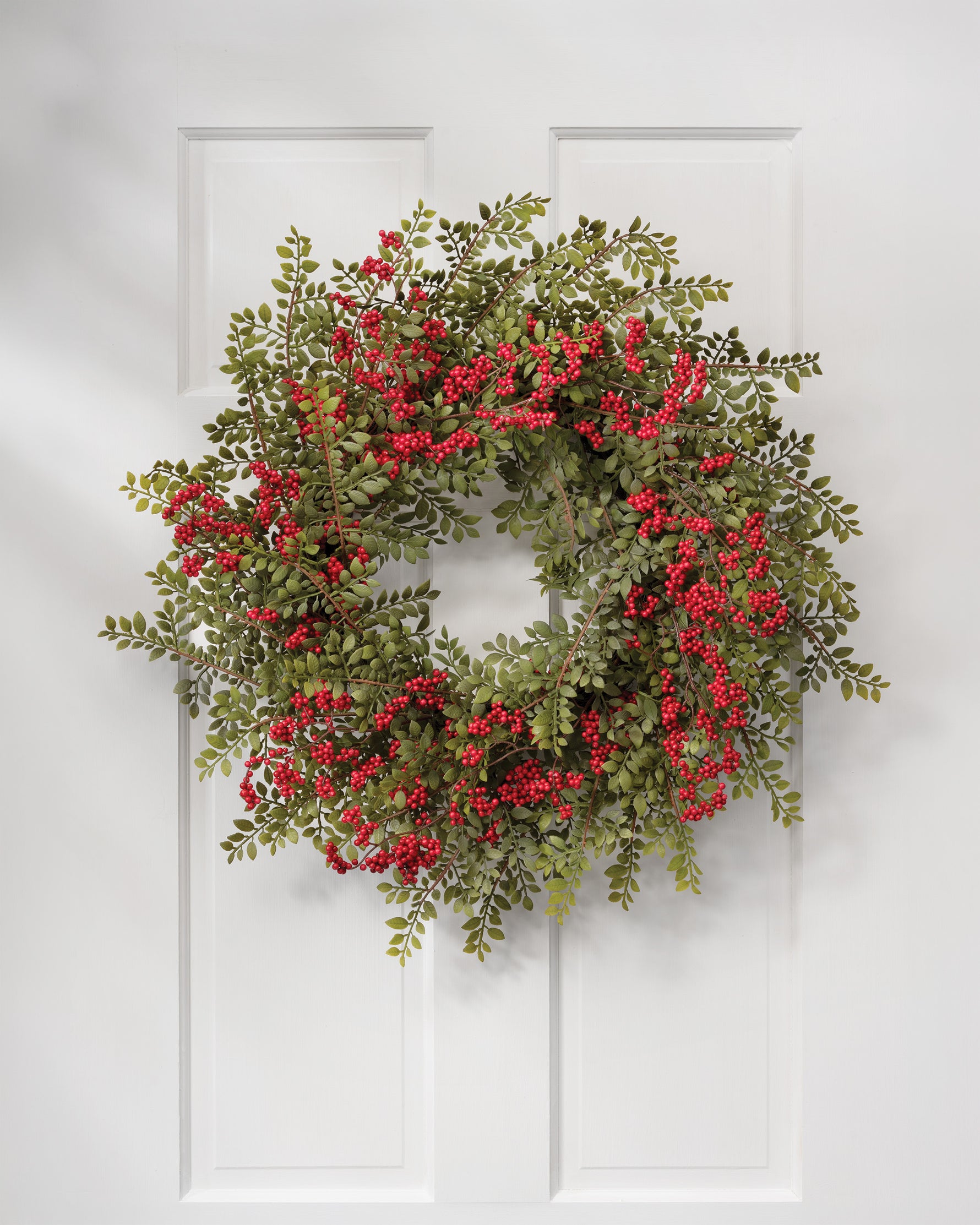 24" Ruscus & Berry Faux Christmas Wreath, hanging on a white wooen door.